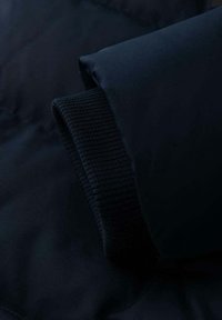 Sezione di giacca imbottita blu navy con polsini in maglia a coste e tessuto liscio. Presenta una texture morbida e leggera e un design minimalista.
