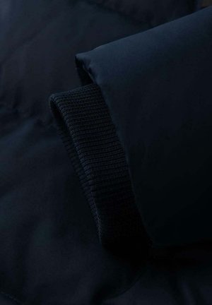 Tmavě modrá péřová bunda s žebrovaným pleteným manžetem a hladkým materiálem. Disponuje měkkou, lehkou texturou a minimalistickým designem.