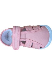 Zapatilla de lona rosa con una tira de Velcro, que presenta un diseño transpirable, suela de goma blanca y tiras elásticas para un ajuste seguro.
