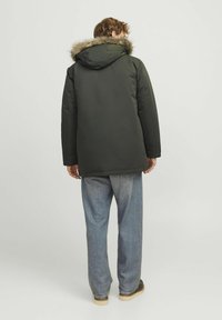 Donkergroene parka met een gevoerde capuchon van bont, lange mouwen en een rechte snit, gecombineerd met lichtblauwe jeans en bruine schoenen.