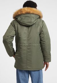 Olivgrüne Parka mit Kapuze und einem beigefarbenen Fellbesatz, gestepptem Textur und Seitentaschen. Bequemer Schnitt mit tailliertem Design.