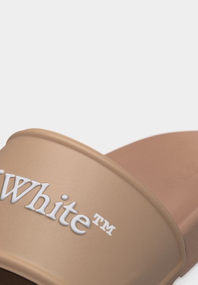 Μπεζ σαγιονάρα με λευκό ανάγλυφο λογότυπο "White TM" στο φαρδύ λουράκι στο πάνω μέρος.