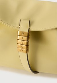 Κίτρινη δερμάτινη τσάντα φάκελος με στρογγυλεμένο καπάκι, που διαθέτει χρυσή μεταλλική λεπτομέρεια με χαραγμένα γράμματα. Λεία υφή και μινιμαλιστικός σχεδιασμός.