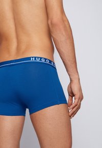 Blaue Boxershorts aus weichem Material. Mit einem weißen, gebrandeten Bund mit dem Text "Hugo Boss". Glatte Textur, eng anliegendes Design.