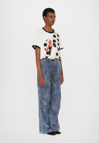 Short-sleeve white t-shirt with black accents and a polka dot design, paired with loose, textured blue denim pants and black flat shoes.
