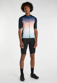 Cyklistický dres má gradientový dizajn v modrej až broskyňovej farbe, krátke rukávy a plný zips. Nosený s čiernymi vypchatými šortkami a topánkami.