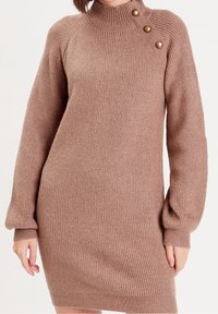 Strikket sweaterkjole i lys brun med høj hals, ribbet tekstur og tre guldfarvede knapper på skulderen. Lange ærmer som snævrer ind ved håndleddet.