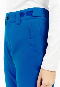 Blauwe stof broek met een gladde textuur, voorzien van een klittenbandsluiting, knoopsluiting en bedrukt merklogo aan de zijkant.