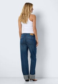 Jeans de denim de perna reta com um tom de azul médio, apresentando um retângulo bege na cintura e um punho contrastante com um interior cinza claro.