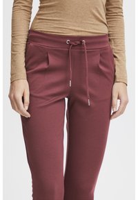 Burgundy joggerbyxor med dragsko i midjan, med två framfållar och en mjuk tygtextur. Matchas med en beige figurnära topp.