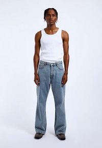 White tank top, light blue loose-fit jeans, and dark shoes. The jeans have a classic five-pocket design with subtle stitching.