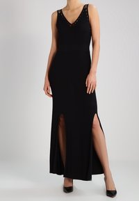 Abito maxi senza maniche nero con scollatura a V profonda, caratterizzato da dettagli con ritagli sulle spalline e spacchi laterali, realizzato in tessuto morbido ed elasticizzato.