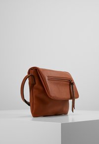 Brun läderaxelväska med klaffstängning, framficka med dragkedja och en texturerad yta. Utrustad med ett kort handtag och kontrasterande sömmar.