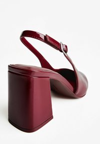 Rote Lackleder-Slingback-Schuhe mit Blockabsatz und silberner Schnalle auf einem weißen Hintergrund.