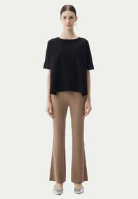 Svart, kortärmad topp med avslappnad passform; matchad med beige, ribbade utsvängda byxor och silverfärgade skor, vilket ger en minimalistisk look.