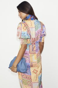 Robe en patchwork coloré aux teintes variées avec des manches bouffantes, un tissu texturé et de la broderie. Associée à une pochette bleue et un foulard à imprimé.