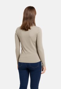 Top a maniche lunghe, aderente, di colore beige chiaro, realizzato in tessuto liscio. Presenta un collo a giro e polsini senza cuciture, abbinato a jeans blu scuro.