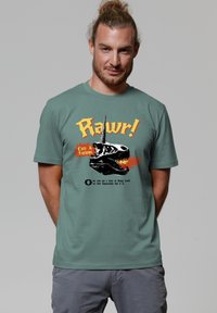 Grünes Baumwoll-T-Shirt mit einem Motiv eines Dinosaurierschädels mit einem Einhornhorn, orangefarbenem Text "Rawr!" und schwarzen Flammenakzenten.