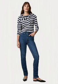 Top a maniche lunghe a righe blu navy e bianche con dettaglio di scollo arricciato, abbinato a jeans aderenti blu e ballerine nere.
