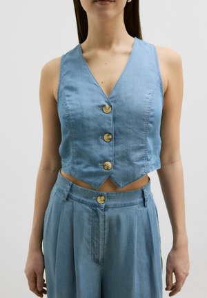 Un gilet cropped bleu clair en denim, doté d'un décolleté en V et de quatre boutons ronds en bois, associé à un pantalon taille haute assorti.