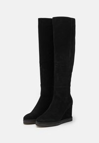 Mustat mokkanahasta valmistetut polven korkeuteen ulottuvat kiilatossut, joissa on sileä pinta, pyöreä kärki ja kevyt korokepohja. Ei näkyviä metalliosia tai kuvioita.