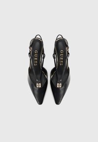 Pantofi cu toc slingback din piele lacuită neagră, cu vârf lung, având accente de hardwear aurii și numele brandului "GUESS" embosat pe talpa interioară.