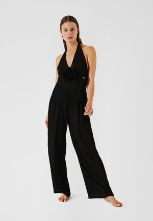 Black halter top with a textured finish and a large flower accent, paired with wide-leg black pants, both made of lightweight fabric.