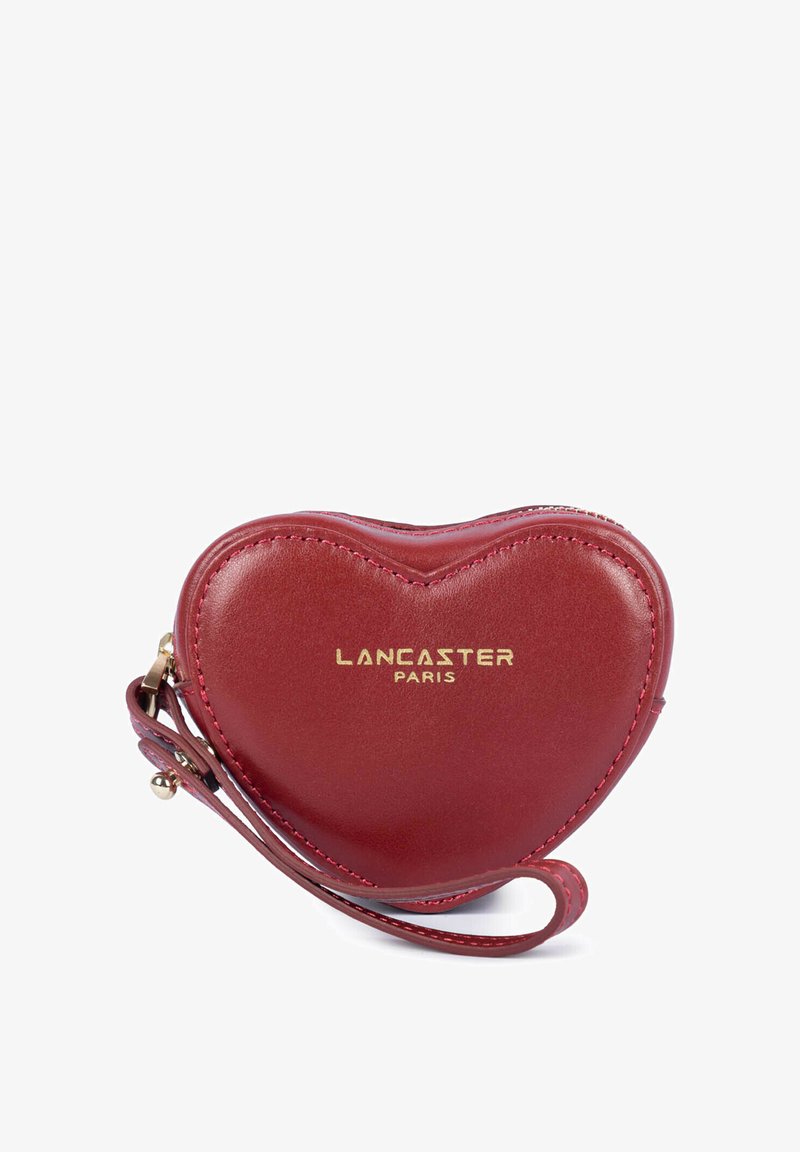 Porte-monnaie en cuir rouge en forme de cœur avec logo doré "Lancaster Paris" et une lanière pour poignet sur fond blanc.