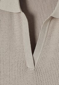 Pull-over en tricot beige clair avec un tissage texturé, présentant un col court et un décolleté en V, mettant en valeur le motif complexe.