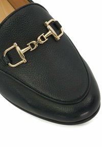 Zwarte leren loafer met een gestructureerde afwerking, voorzien van een gouden kettingaccent over de voorkant en een ronde teenontwerp.