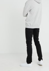 Sudadera gris, jeans negros y zapatillas blancas. La sudadera tiene un corte estándar y un bolsillo canguro, mientras que los jeans son de corte ajustado.