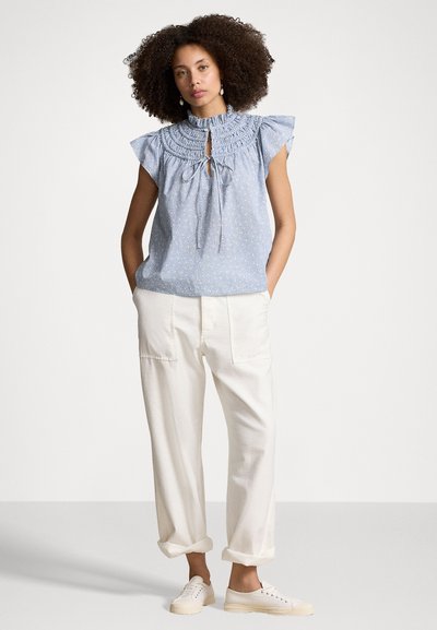 Lichtblauw bloemenblouse met gerimpelde halslijn en keyhole-detail, gecombineerd met crèmekleurige wijde broek en witte sneakers.