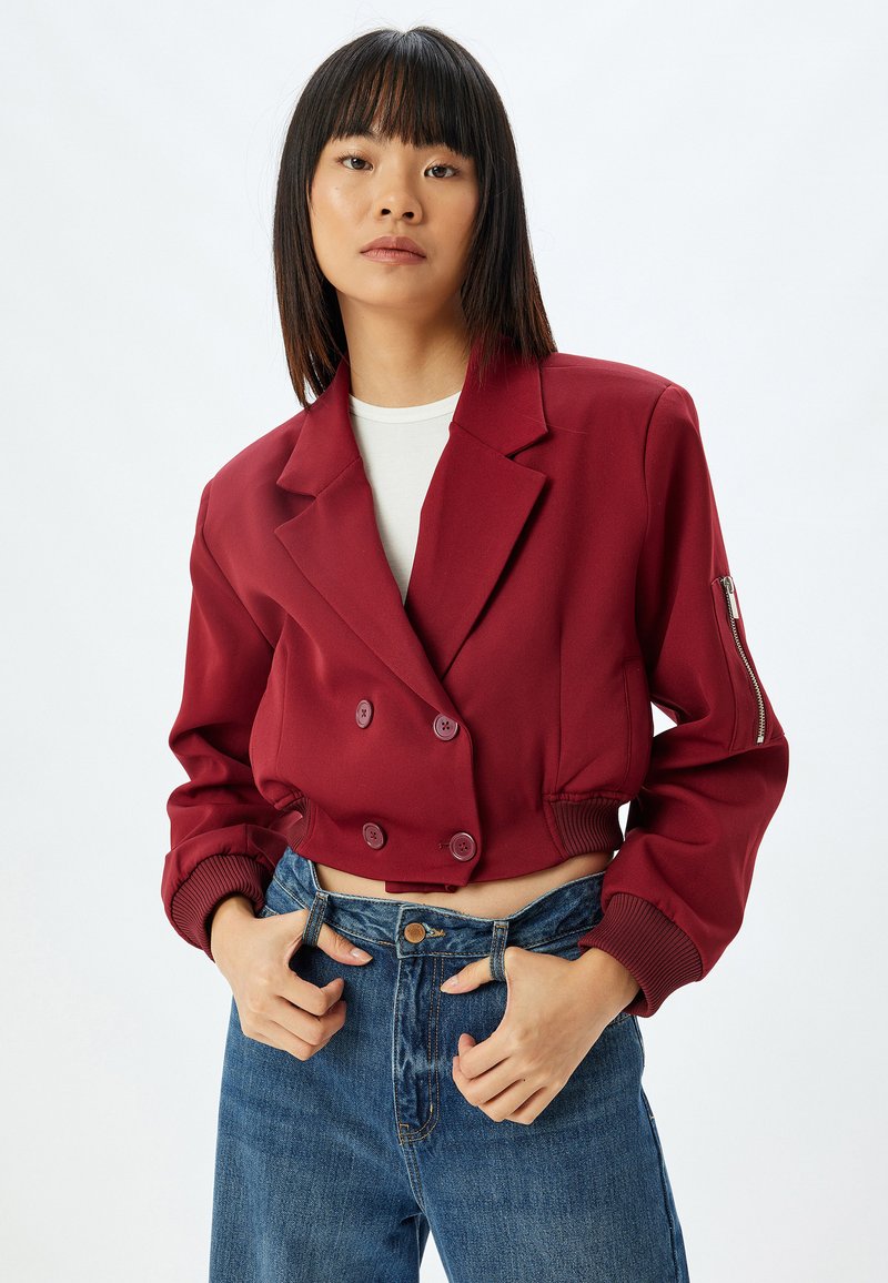 Bordeauxfarvet cropped dobbeltbrystet jakke med knapper og ribbede mansjetter, parret med højtaljede denimjeans. Glat tekstur, skræddersyet design.