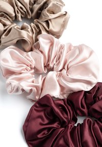 Tre scrunchies in satin color beige, rosa chiaro e bordeaux. Il tessuto è liscio con una finitura lucida, mostrando morbidi tessuti arricciati.