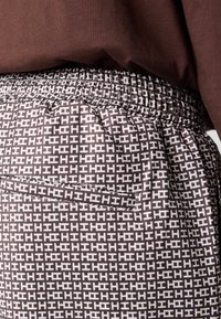 Pantalons avec taille élastique marron et un motif géométrique blanc sur toute la surface. Dotés d'une poche arrière zippée pour le rangement.