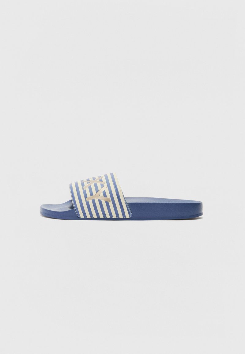 Blå sklidedaller med en stripet, lyseblå og kremfarget band med logo. Glatt overflate, flat såle og åpen tå-design.