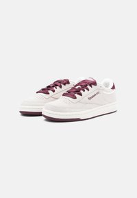 Białe zamszowe sneakersy z bordowymi satynowymi sznurówkami i akcentami, okrągły nos, oraz teksturowana podeszwa, z logo marki po boku.