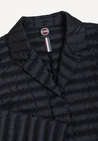 Mustast tepitud jope, millel on kraelappidega krae, horisontaalsed õmblused ja Colmar Originals silt, millel on krae siseküljel tumepunase, halli ja valge triibulise kanga aas.