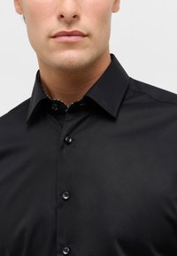 Camicia nera con colletto classico, tessuto liscio, chiusura a bottoni e colletto interno con motivo a contrasto. Presenta bottoni scuri.