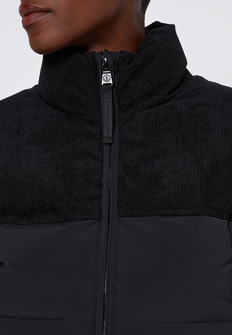 Schwarze Jacke mit hohem Kragen, der im oberen Teil eine gerippte Textur und im unteren Bereich glattes Material aufweist, mit einem Reißverschluss vorne.