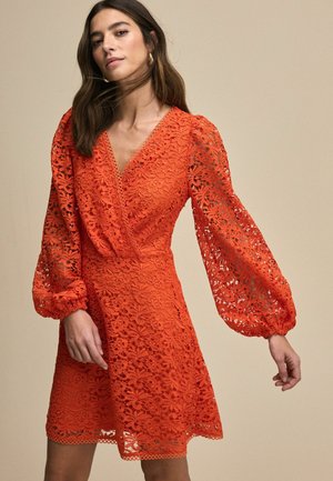 Lace dress in vibrant orange with a V-neck, balloon sleeves, and intricate floral patterns. Hem features scalloped edges.