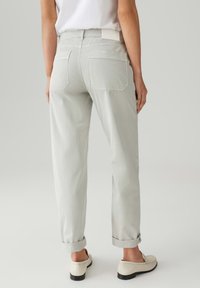 Pantaloni grigi chiari con vestibilità ampia, risvolti, due tasche posteriori e un'etichetta in vita, abbinati a scarpe bianche senza lacci.