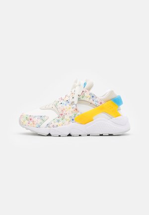 White sneakers with multicolored floral patterns, featuring a yellow accent and a blue heel. Crafted from a smooth material with a textured sole.