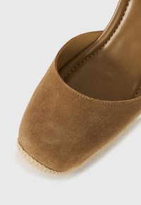 Καφέ καστόρινο γυναικείο παπούτσι με ψηλό τακούνι, στρογγυλεμένη μύτη και φυσική διακόσμηση από σχοινί στη σόλα. Λείο εσωτερικό επένδυση και ραμμένες άκρες.