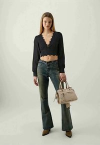 Top cropped nero con bordi scallop, jeans flare blu, borsa beige e tacchi a punta marroni su uno sfondo chiaro.