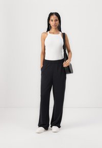 Valge ribadega top, mis on seotud mustade elastse vööga laiad püksid. Mudel hoiab väikest musta õlakot ja kannab valgeid spordijalatsid.