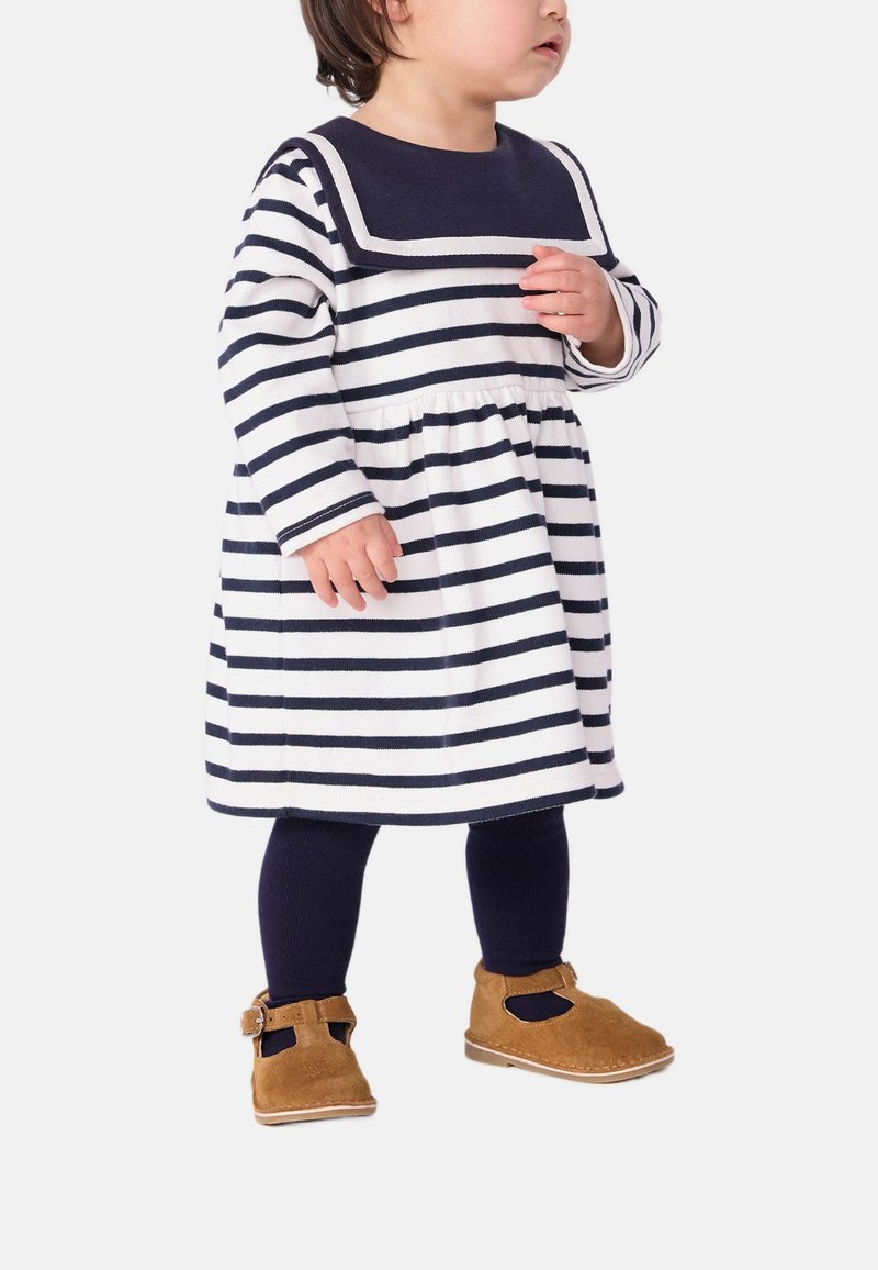 Robe rayée bleu marine et blanche, décolleté carré, taille froncée, assortie à des collants bleu marine et des chaussures en suède marron avec une boucle.