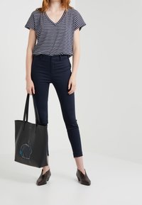 Gestreepte marineblauwe en witte V-hals top, marineblauwe aansluitende broek, zwarte tas met een konijnontwerp, en bruine gestructureerde hoge hakken.