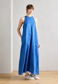 Blå linnmaxiklänning med hög halsringning och ärmlös design, som har en avslappnad passform. Matchad med vita sneakers och ljusa strumpor.