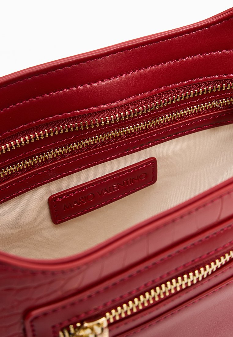Interno di una borsa a tracolla rossa in pelle con cerniere dorate, caratterizzato da una texture liscia e un'etichetta di marca. Rivestita in tessuto beige.